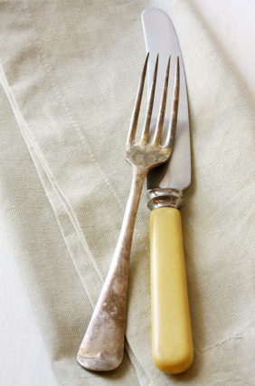 Vintage knife and fork on linen napkin. Bone-handled knife and tarnished silver fork.